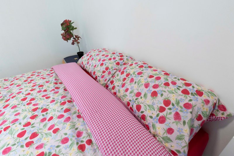 Bedroom with floral patterned bedding, pink gingham sheet, and potted plant on pillow