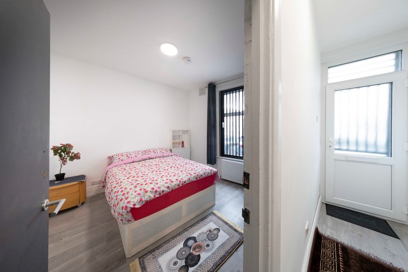 Small bedroom with single bed, pink bedding, wooden nightstand and entrance door