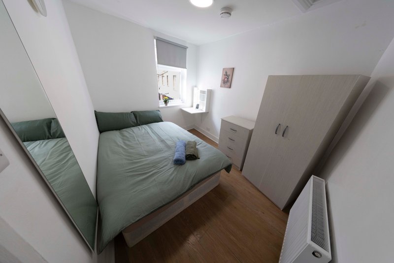 Bright bedroom with double bed, green bedding, wooden floor, wardrobe and window