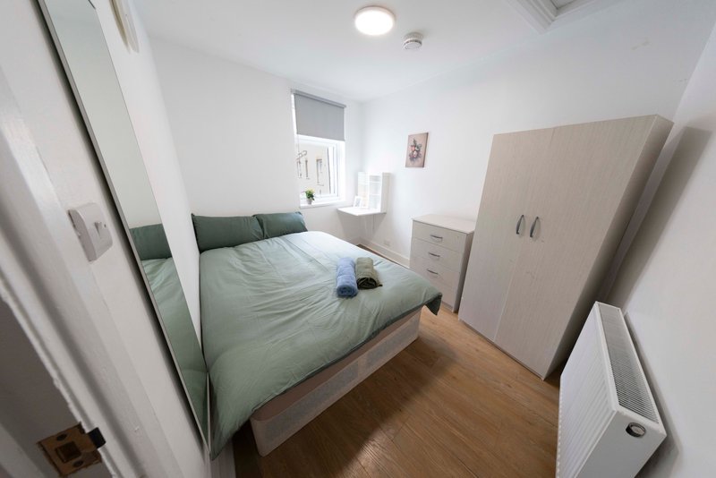 Compact bedroom with double bed, green bedding, wooden floor and white wardrobe