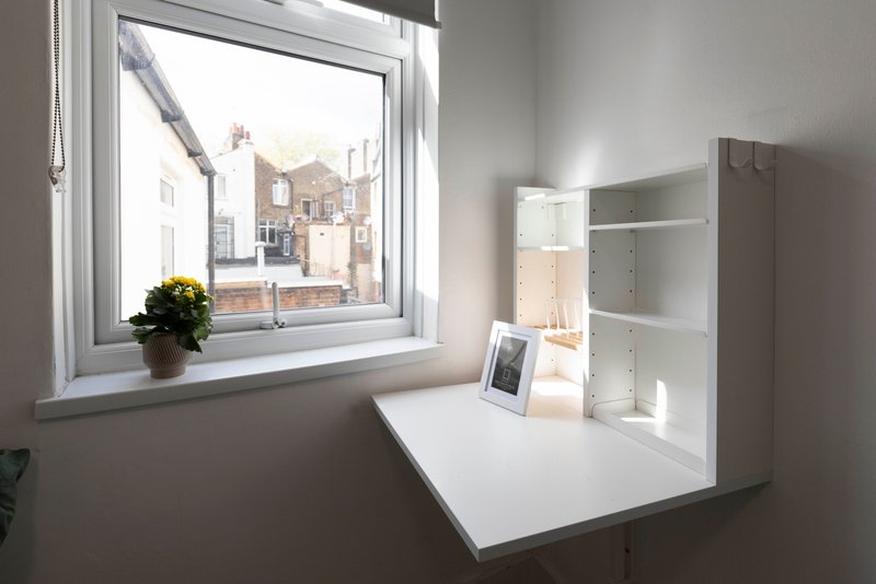 Bright workspace with white desk, window overlooking street, potted plant and shelving unit