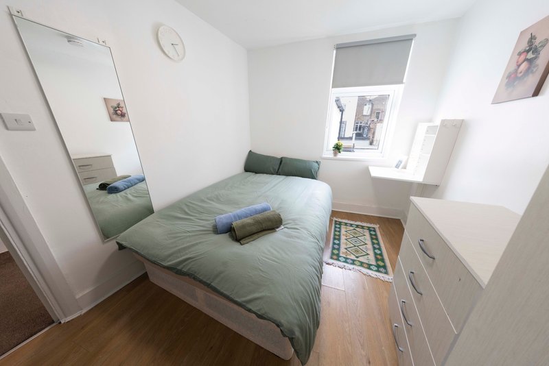 Compact bedroom with single bed, green bedding, full-length mirror, and wooden flooring