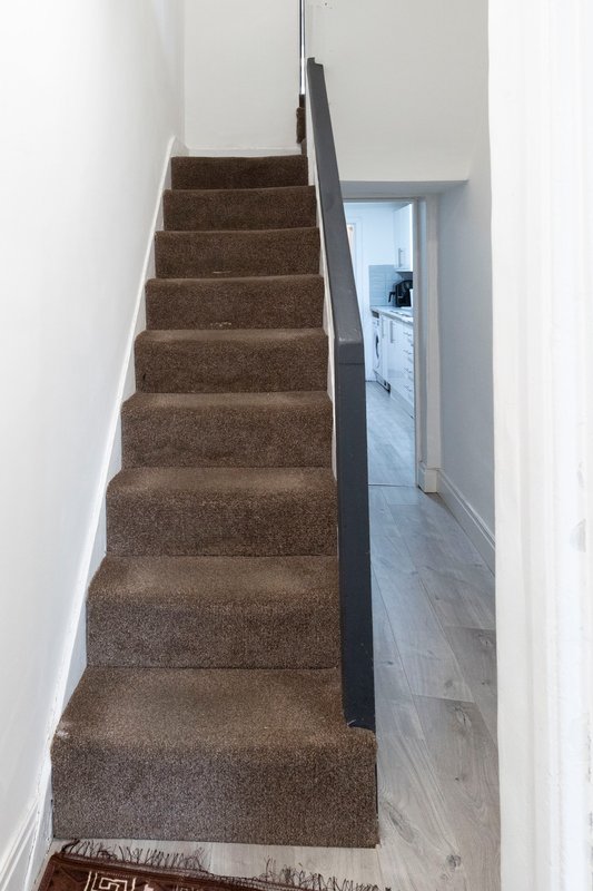 Staircase with brown carpet, black handrail, white walls and hallway view