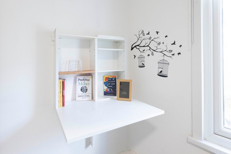 White wall-mounted desk with shelving, books, and decorative branch wall decal