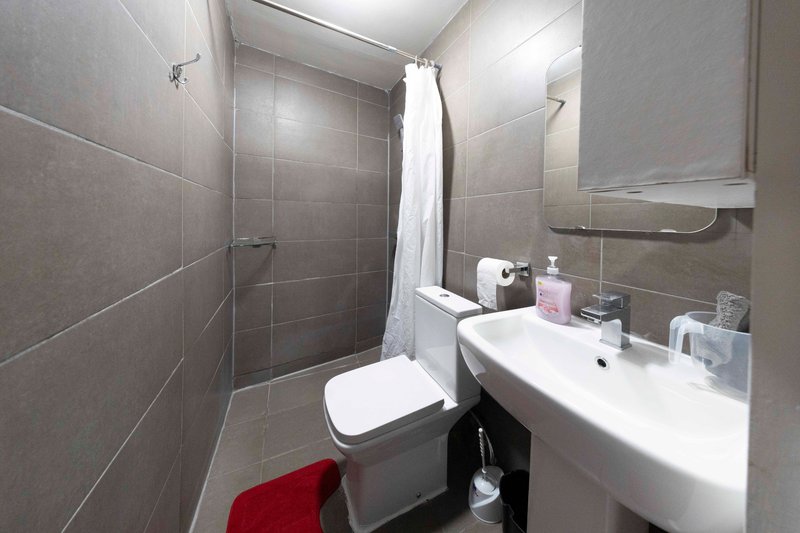 Modern bathroom with gray tiled walls, white sink, toilet, and shower enclosure with curtain