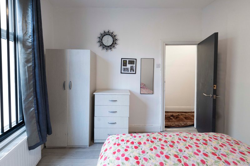 Bright bedroom with pink patterned bed, white wardrobe, chest of drawers, and decorative wall clock