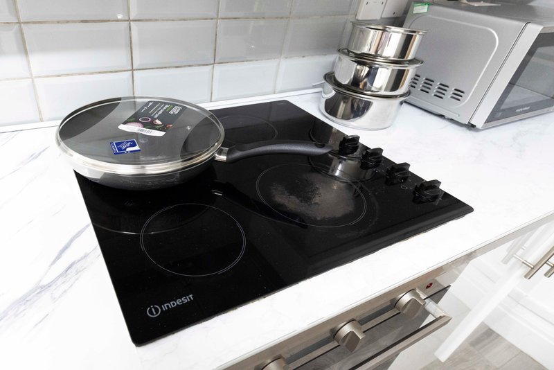 Modern kitchen countertop with induction hob, stainless steel cookware, and white tiled backsplash