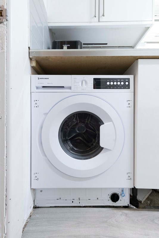 Built-in washing machine under wooden countertop with white cabinetry above