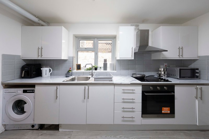 Modern white kitchen with grey tile splashback, integrated appliances, and natural light from window