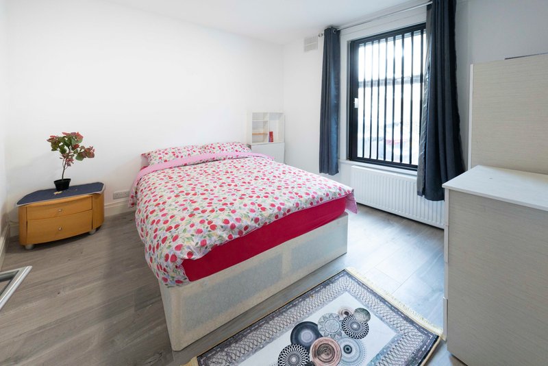 Bright bedroom with single bed, wooden dresser, potted flowers, and glass door to garden