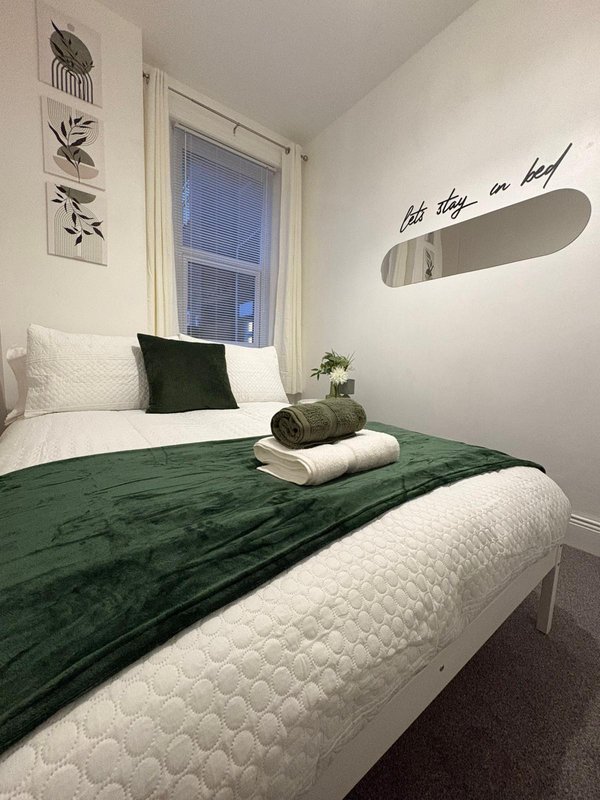 Bedroom with double bed, green bedding, black cushion, window, and wall decor