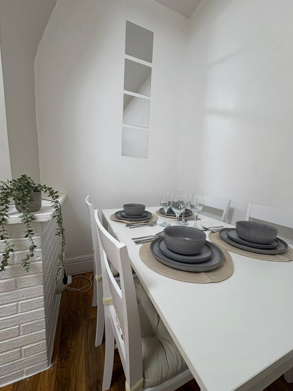 Minimalist dining room with white table, chairs, place settings and small potted plant
