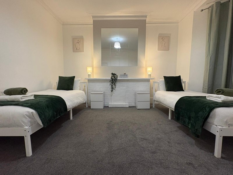 Twin bedroom with two single beds, dark green bedding, white wooden frame, central vanity mirror and lamp