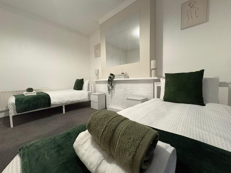 Modern bedroom with two single beds, green cushions, white bedding and shared bathroom area