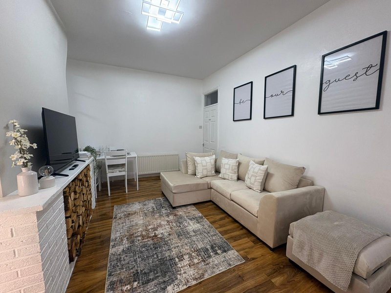 Living room with cream sofa, TV, wooden floor, framed wall art and area rug