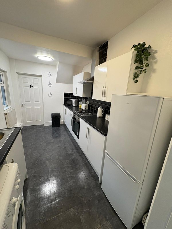 Galley kitchen with white cabinets, black countertop, stainless steel appliances and dark flooring