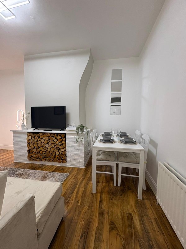 Open-plan living area with TV on fireplace, dining table, wooden flooring and white walls
