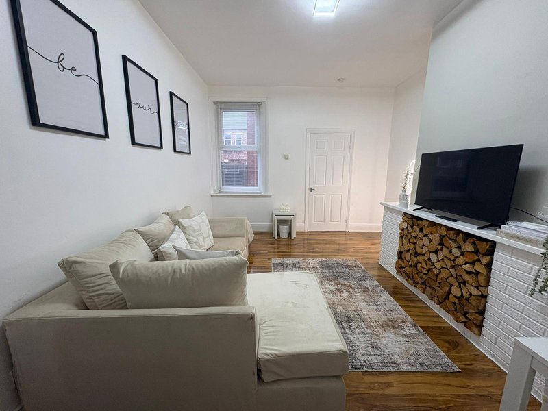 Bright living room with cream sofa, TV, firewood storage and wooden flooring