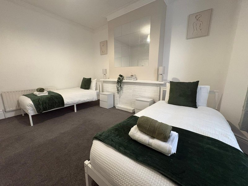 Shared bedroom with three single beds, dark carpet, white bedding, and bathroom vanity mirror