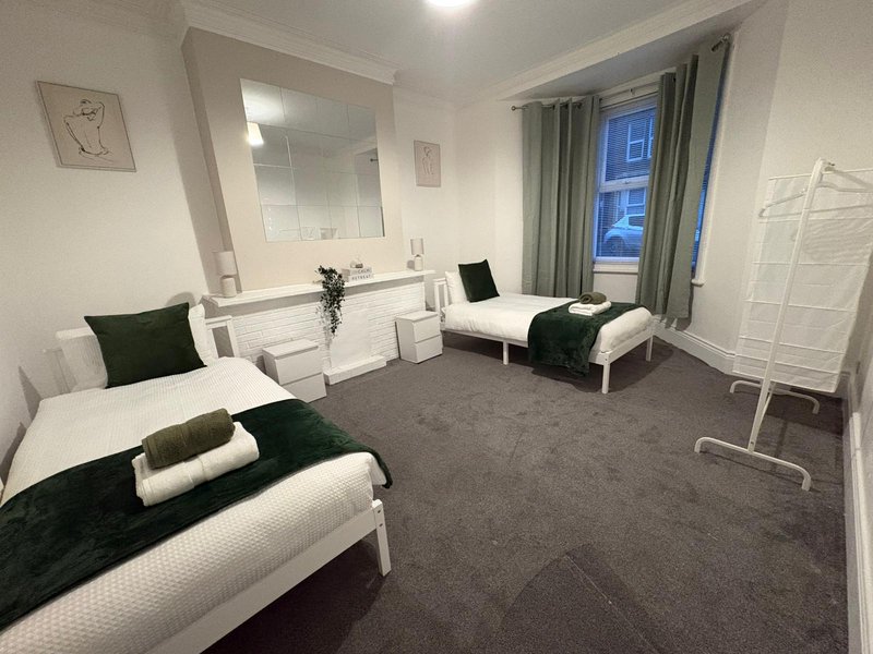 Spacious bedroom with two single beds, mirror, dark carpet, and large window with curtains