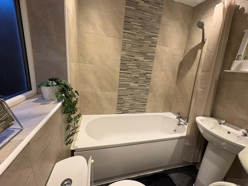Modern bathroom with bathtub, sink, toilet, tiled walls and decorative plant
