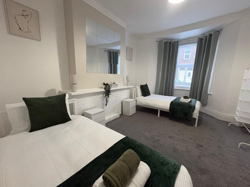 Bright modern bedroom with two single beds, mirror, sink area and green curtains