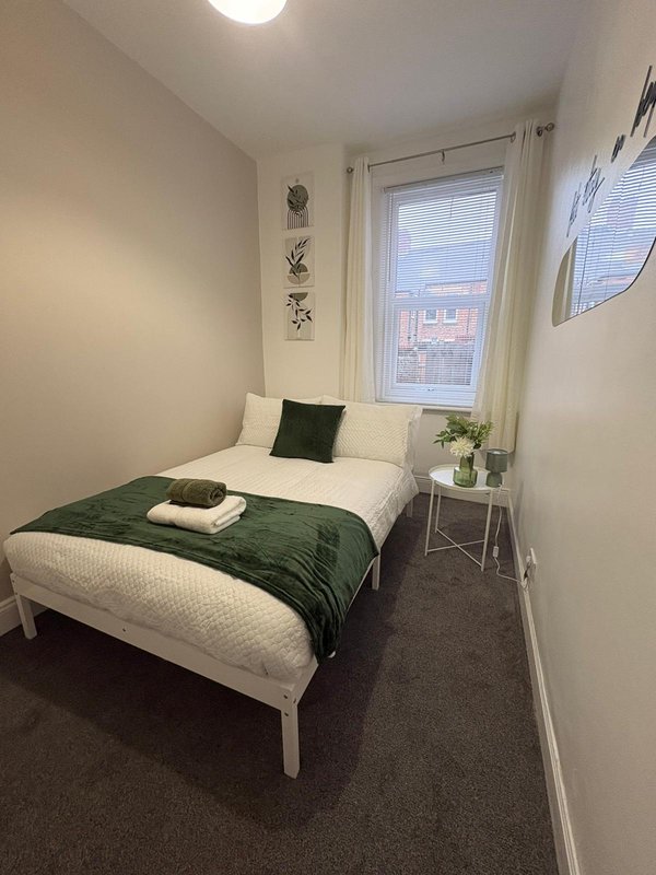 Bedroom with single bed, green bedding, window with blinds, and potted plant on side table
