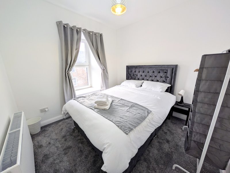Modern bedroom with double bed, gray headboard, white bedding, and window with gray curtains