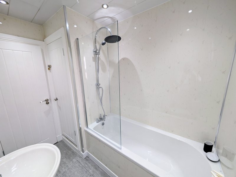 Modern bathroom with white toilet, glass-enclosed bathtub, rainfall shower head and light gray floor
