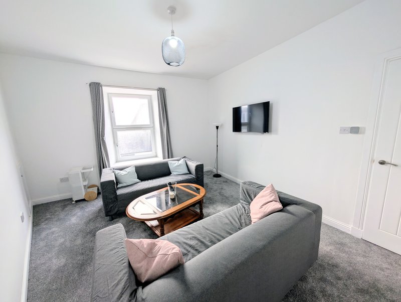 Modern living room with grey sofa, wooden coffee table, wall-mounted TV and window with curtains