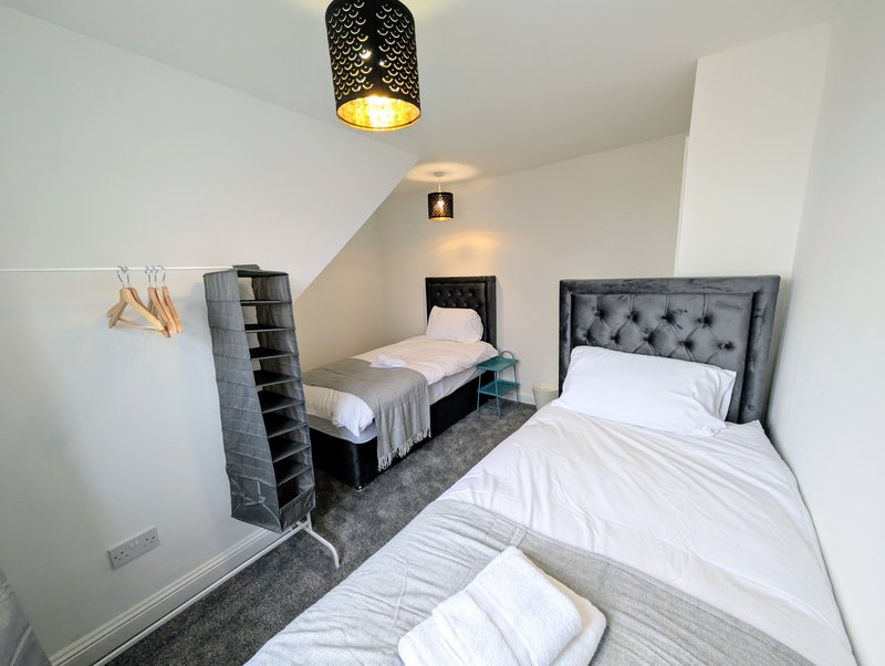 Bedroom with two single beds, gray upholstered headboards, white bedding, and pendant ceiling light