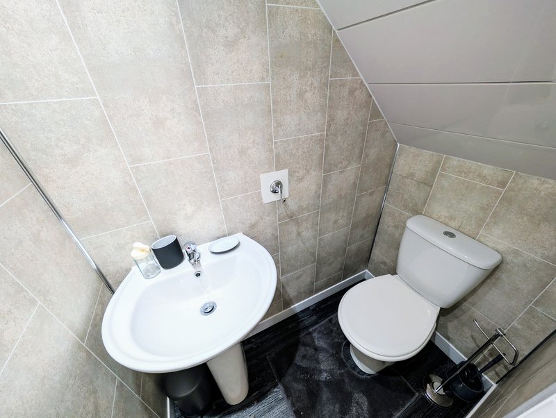 Small bathroom with wall-mounted sink, toilet, and beige tile walls