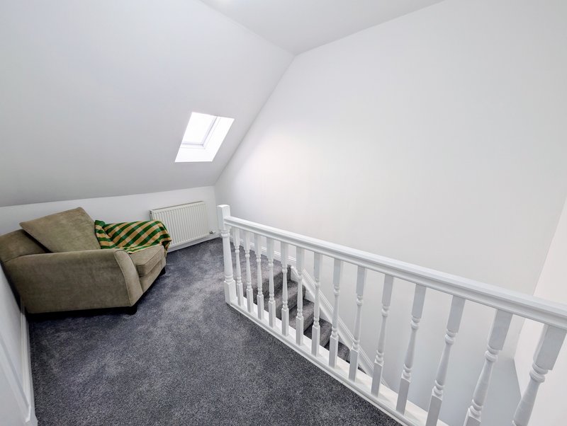 Attic bedroom with skylight, gray carpet, armchair with cushions, and white crib