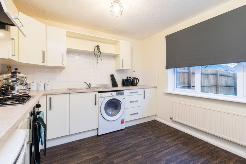 Modern kitchen with white cabinetry, washing machine, dark wood flooring and window