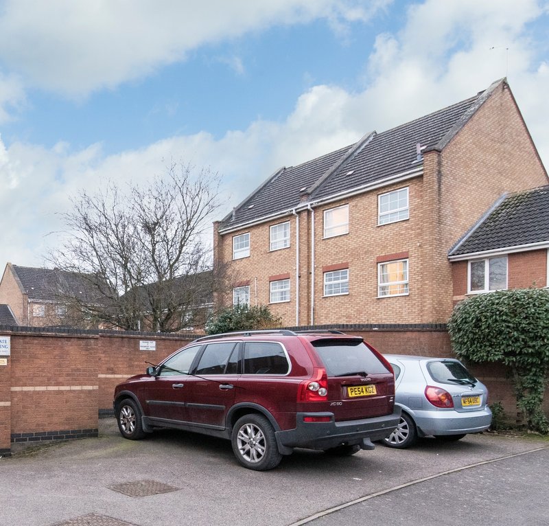 Brick residential building with driveway, parked vehicles and front garden