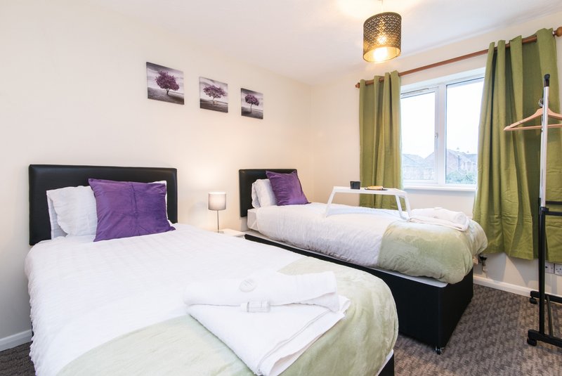 Twin bedroom with two single beds, purple cushions, green curtains and wall art