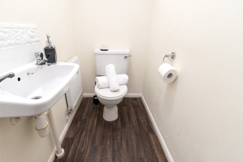 Small bathroom with white sink, toilet, towel rail and dark wood flooring