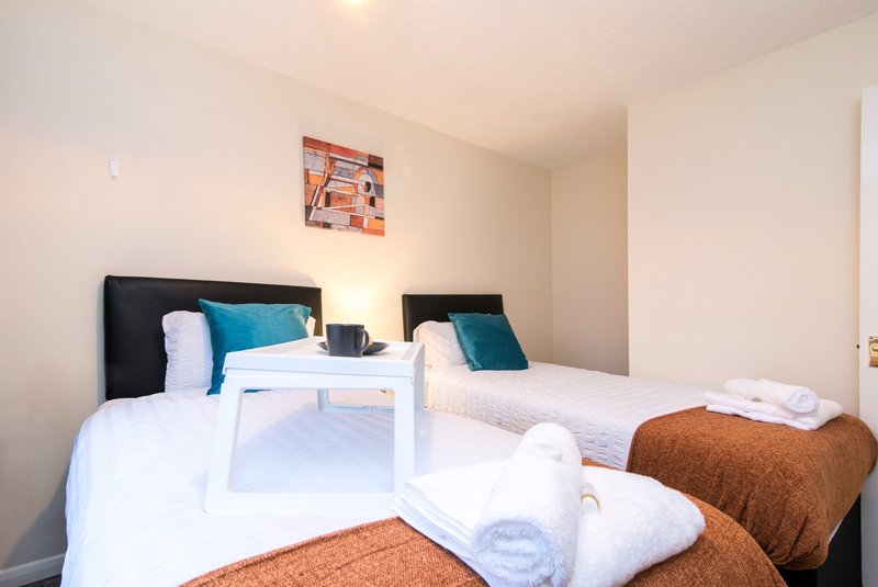 Bright bedroom with two single beds, white bedding, teal cushions, and small white table between them