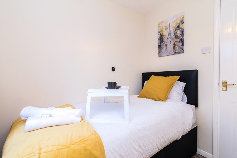 Modern bedroom with black bed frame, white bedding, yellow cushion and throw, bedside table with lamp