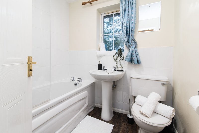 Clean bathroom with pedestal sink, toilet, bathtub and window with blue curtains