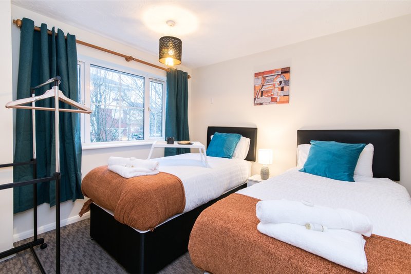 Twin bedroom with two beds, blue cushions, teal curtains and pendant lamp