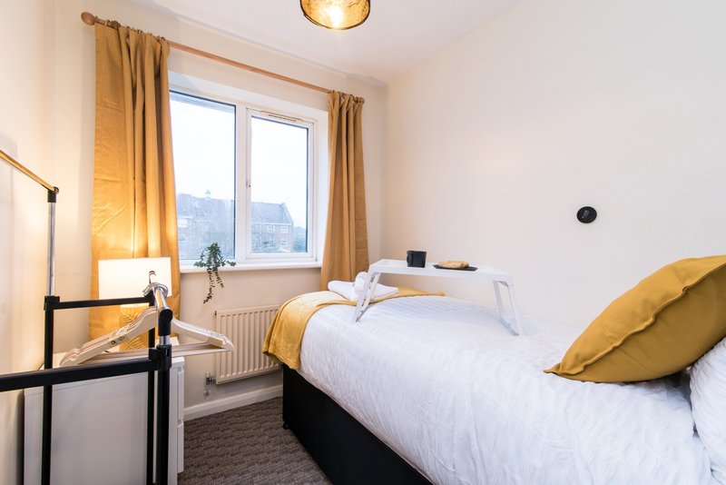 Bright bedroom with two single beds, gold curtains, window view and floor lamp