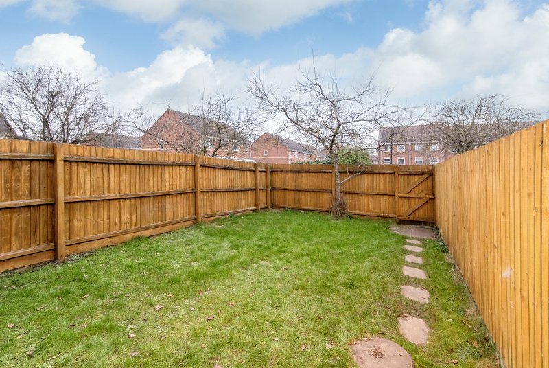 Enclosed garden with wooden fence, green lawn, stepping stones and bare trees