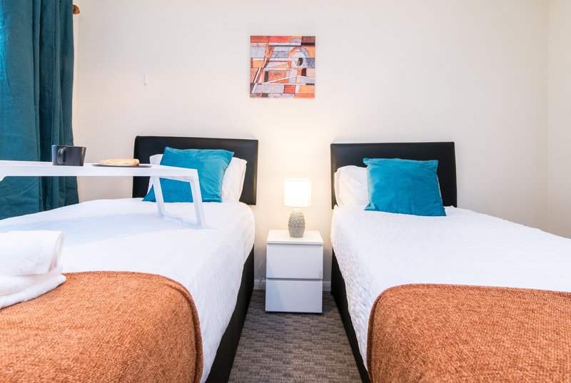Twin bedroom with two single beds, black headboards, turquoise pillows and orange throws