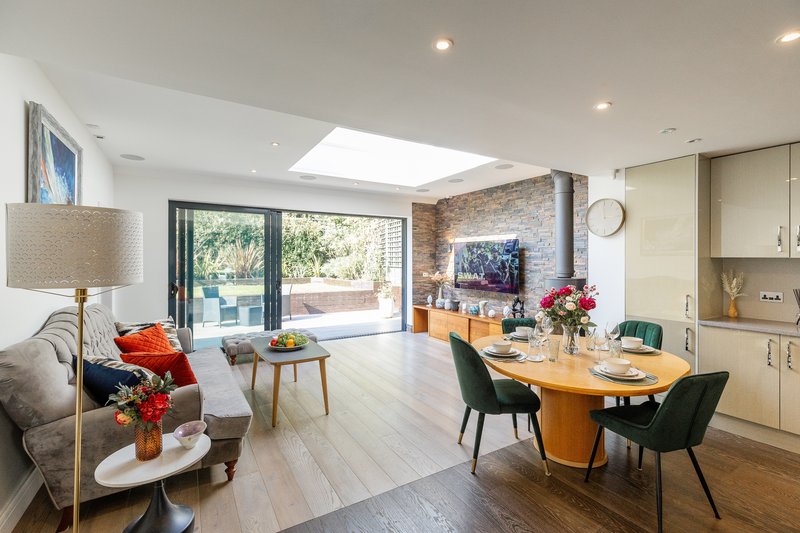 Open-plan living and dining room with wooden table, modern kitchen, sofa, and garden views