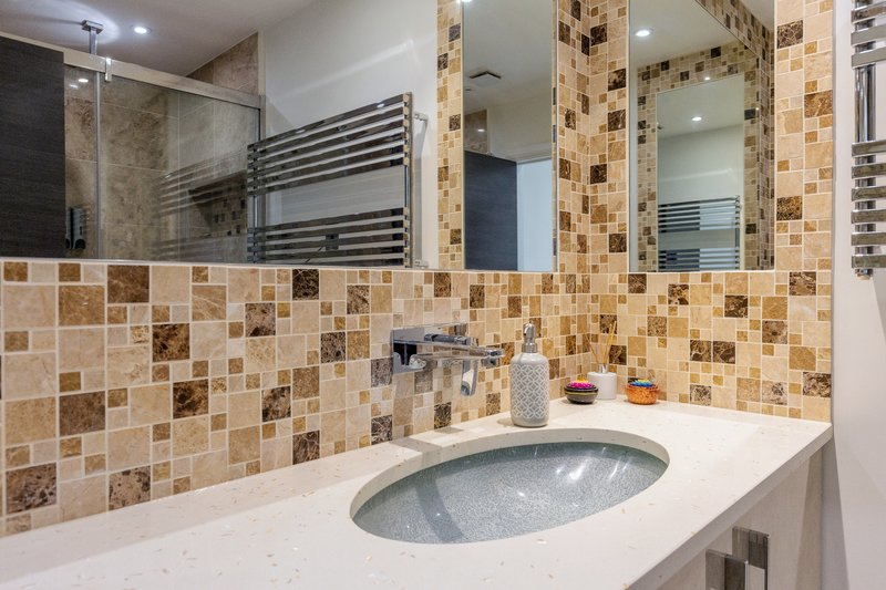 Modern bathroom with mosaic tile backsplash, oval sink, mirror and heated towel rail