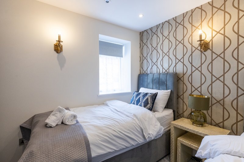 Bedroom with double bed, patterned wallpaper, wall sconces, and window with natural light