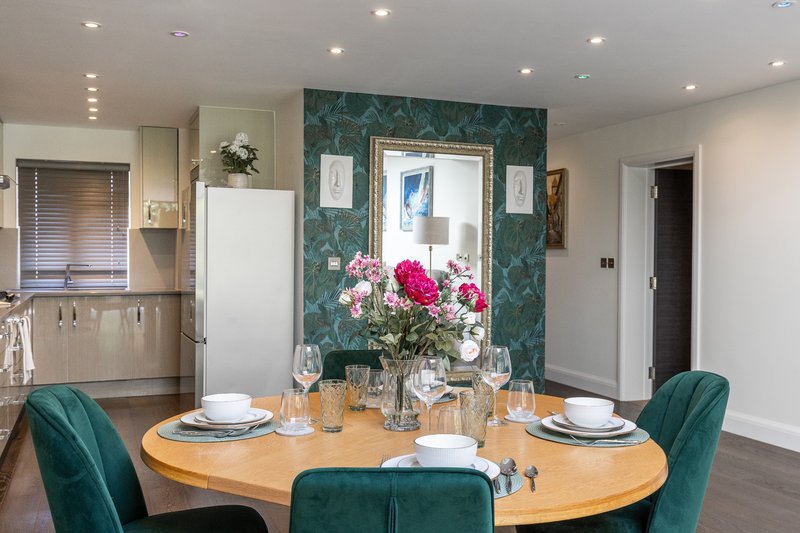 Modern dining room with oval wooden table, teal velvet chairs, floral centerpiece and mirror