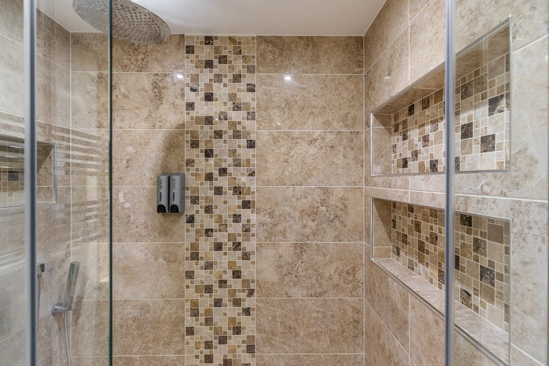 Luxury bathroom with walk-in shower, travertine tiles, mosaic accent strip and built-in shelving