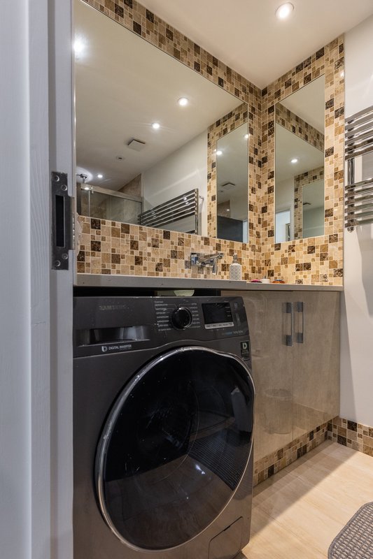 Modern bathroom with black washing machine, mosaic tile backsplash, mirrors and recessed lighting